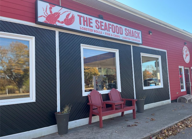 The Seafood Shack storefront on St. Peters Road in Morell, PE — the black-and-red building with the lobster sign and a red bench out front